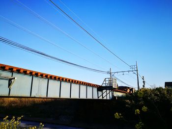 Low angle view of electricity pylon against clear blue sky