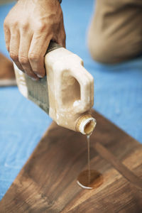 Cropped image of carpenter pouring oil on triangle shaped wood at workshop