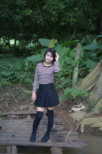 Portrait of smiling young woman standing on pier against trees in forest