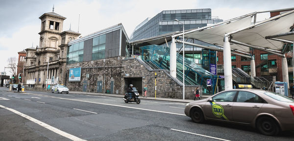 Cars on road by buildings against sky in city