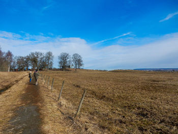 People walking on footpath by field against sky