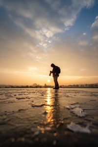 Silhouette man standing on beach against sky during sunset