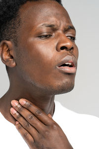 Black man touches fingers of sore throat, thyroid gland. painful swallowing, tonsil, angina concept.
