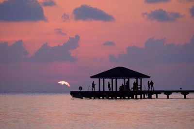 Silhouette people on gazebo over sea against sky during sunset