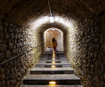 Rear view of woman walking on staircase in illuminated tunnel