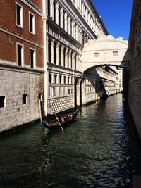 Gondola on canal amidst buildings in city during sunny day