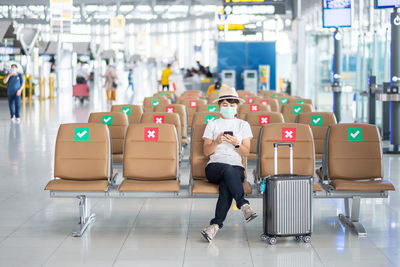 Full length portrait of man sitting at airport