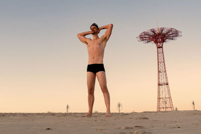 Shirtless man standing at beach against sky