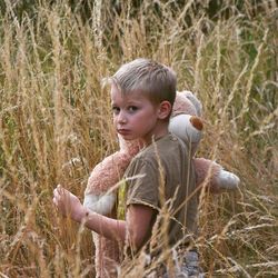 Portrait of boy with teddy bear standing on field