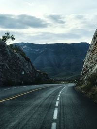 Empty road leading towards mountains against sky