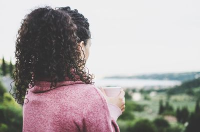 Rear view of woman holding coffee cup against clear sky