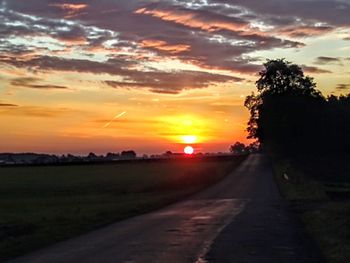 Road by silhouette trees against sky during sunset