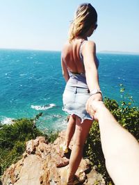 Rear view of young woman standing by sea against clear sky