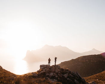 People standing on mountain against sky at sunset