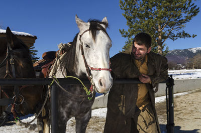 Man with horse standing in ranch against clear sky