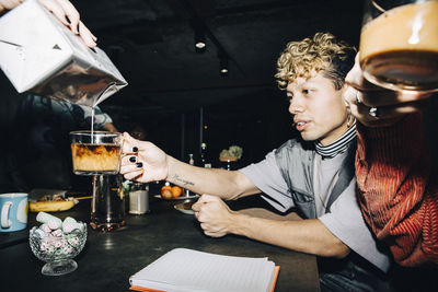 Young businesswoman pouring milk in coffee for coworkers at workplace