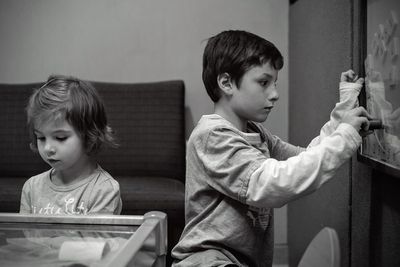 Side view of boy playing with toy while standing by sister at home