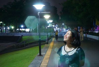 Woman looking away while standing on street at night