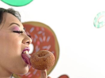 Close-up of woman licking sweet food against wall