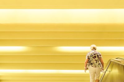 Rear view of woman standing against yellow wall