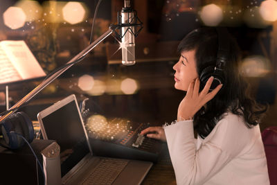 Side view of woman wearing headphone sitting at recording studio