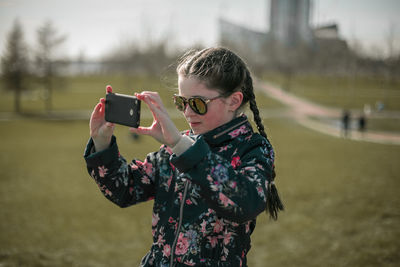 Young woman photographing with mobile phone at park