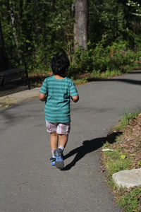 Rear view of boy running on road against trees
