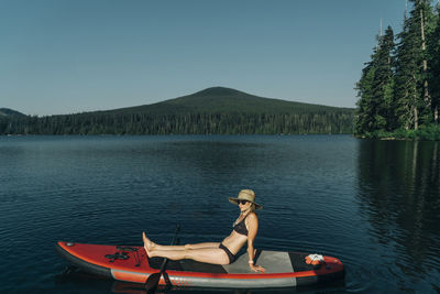 A young woman sits on a sup on lost lake in oregon.