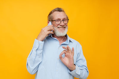 Portrait of young woman talking on phone against yellow background