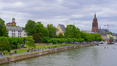 Buildings by river against cloudy sky