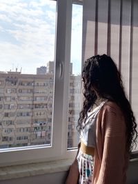 Side view of young woman looking through window