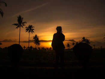 Silhouette man standing on field against sky at sunset