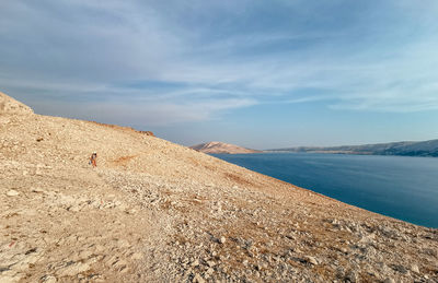 Tiny person walking on path on rocky coastline with view of deep blue sea on pag island in croatia.