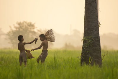 Shirtless boys playing while standing on grassy field against clear sky