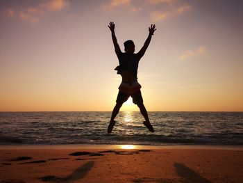 Silhouette man jumping at beach against sky during sunset