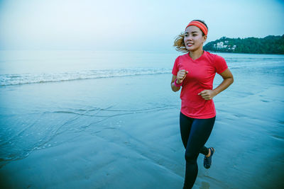 Full length of smiling woman standing on sea shore against sky