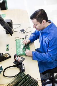 Mature male electrician working on circuit board at desk in factory