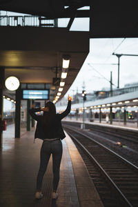 Rear view of young woman holding string light standing at railroad station platform