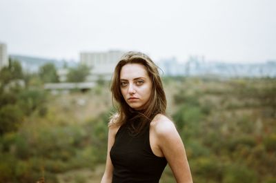 Portrait of beautiful young woman standing on grassy field against clear sky