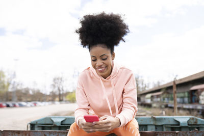 Smiling woman using smart phone while sitting outdoors