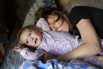 Mother sleeping with toddler daughter on bed at home