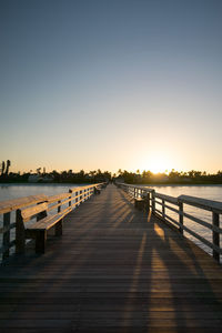 Wooden pier on sea against clear sky during sunset