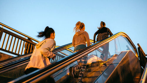 Women friends training running up escalator in city on sunset