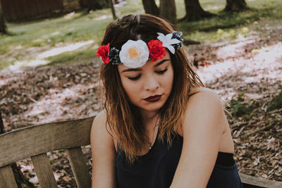 Close-up of young woman wearing flowers while sitting on bench at park