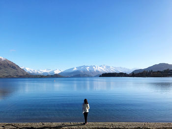 Rear view of woman standing by lake against sky