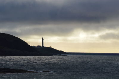 Lighthouse by sea against sky during sunset