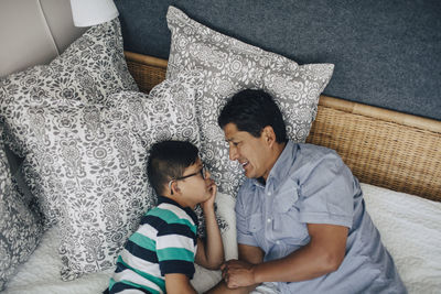 High angle view of father talking to son while lying on bed at home