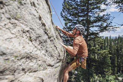 Man holds on to rock with fingertips while climbing with a rope