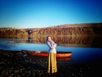 Portrait of woman standing by lake against clear blue sky