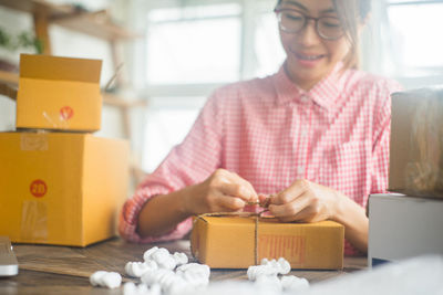 Young woman tying string on cardboard box at home